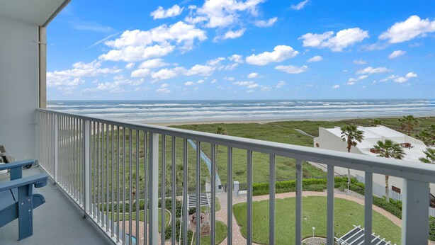 Ein Balkon mit Blick auf das Meer und eine angelegte Grünfläche mit Wegen und Sitzgelegenheiten.
