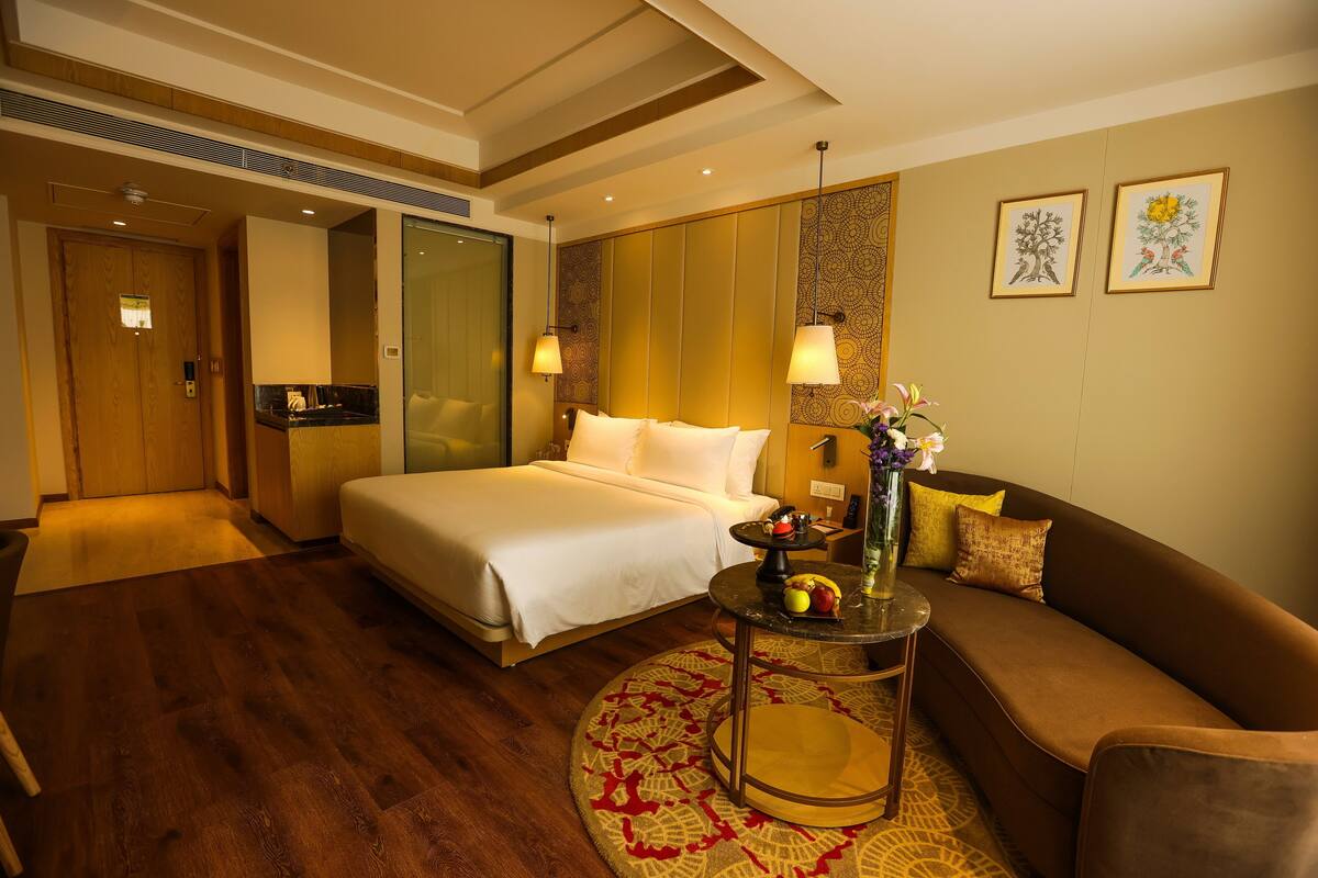 A hotel room with a bed, a sofa, a small table, and a decorative vase.