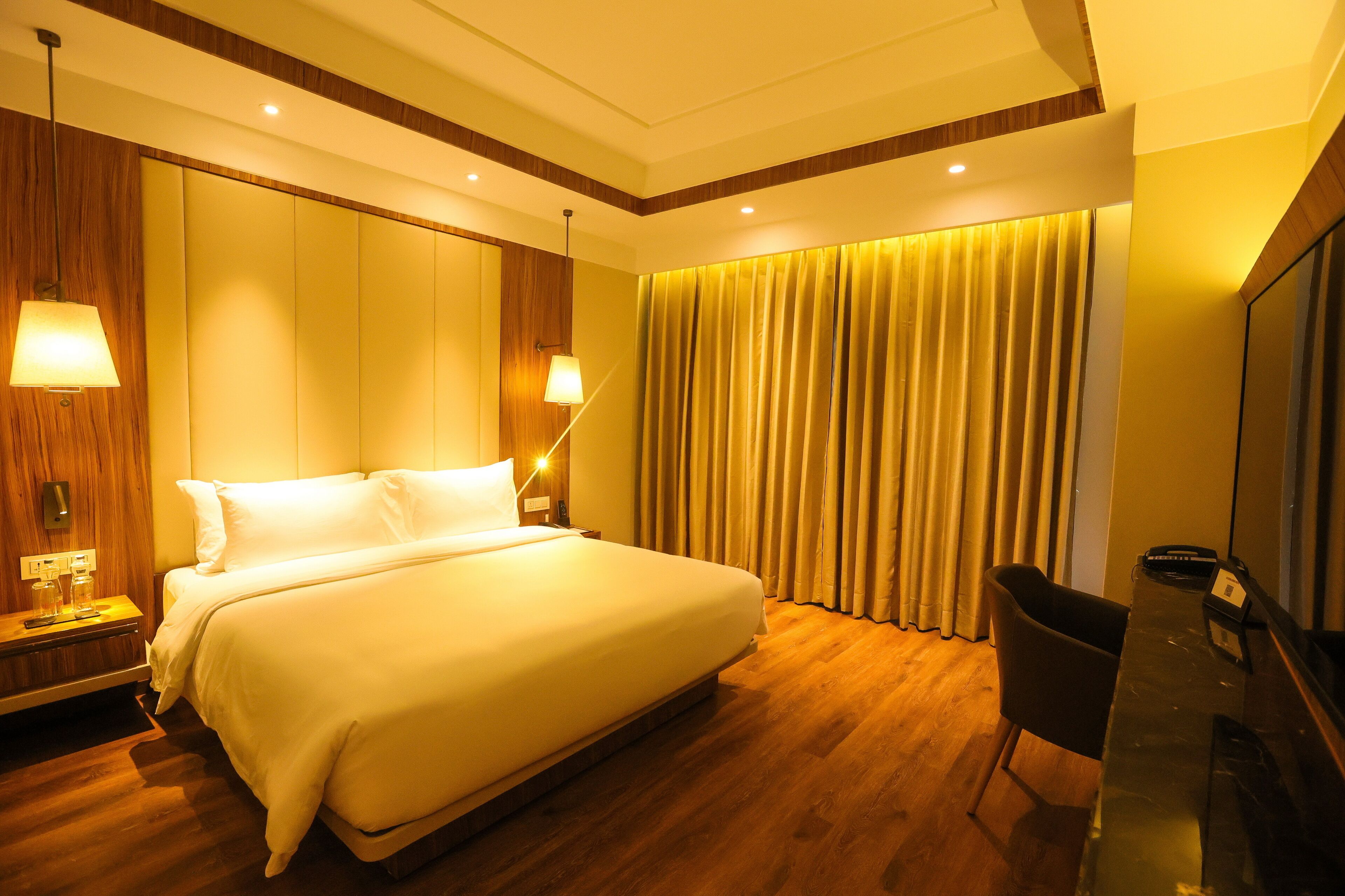 A hotel room with a large bed, wooden paneling, a desk with a chair, and a TV.