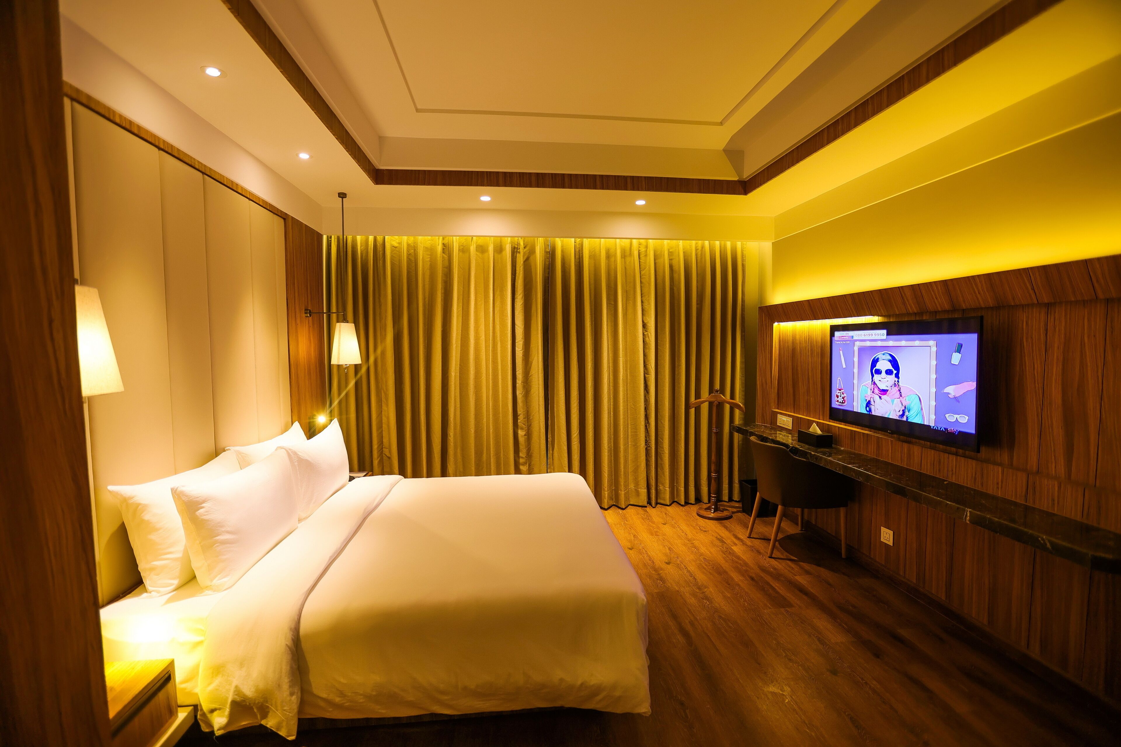 Ein Hotelzimmer mit einem großen Bett, einem Schreibtisch und einem Flachbildfernseher, mit Vorhängen im Hintergrund.