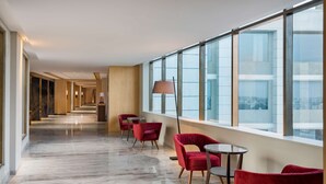 A hotel corridor with red chairs, a lamp, and large windows offering a view of the city. - Radisson Bhopal (Bhopal)