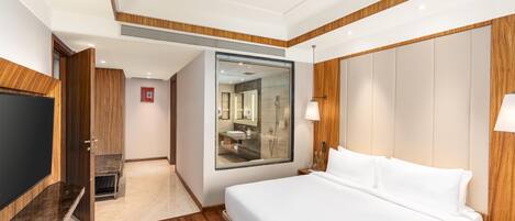 Habitación de hotel con una cama grande, televisión, baño con espejo y paneles de madera.