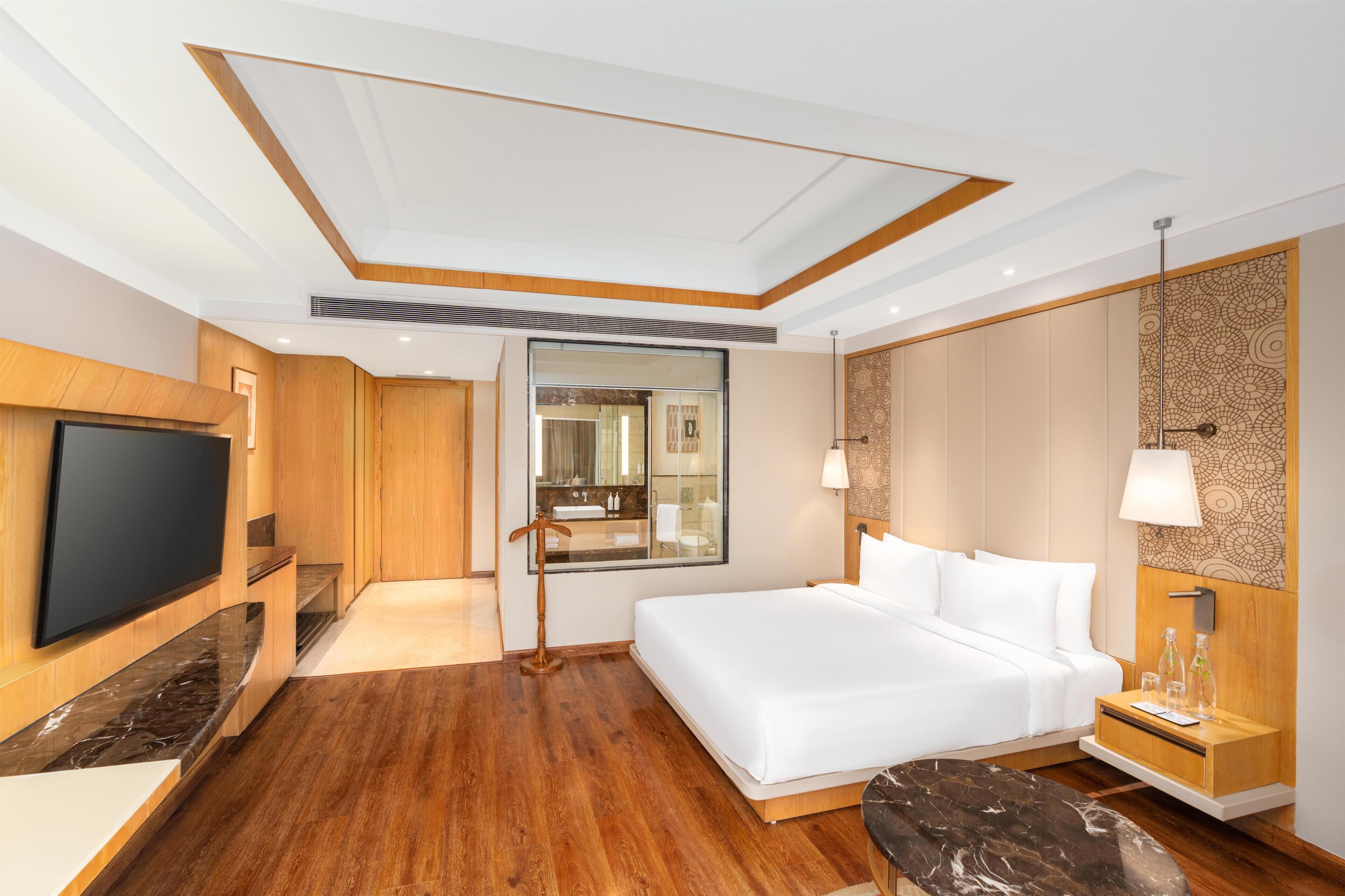 Une chambre d’hôtel avec un grand lit, une télévision, une salle de bain avec un miroir et un plancher en bois.
