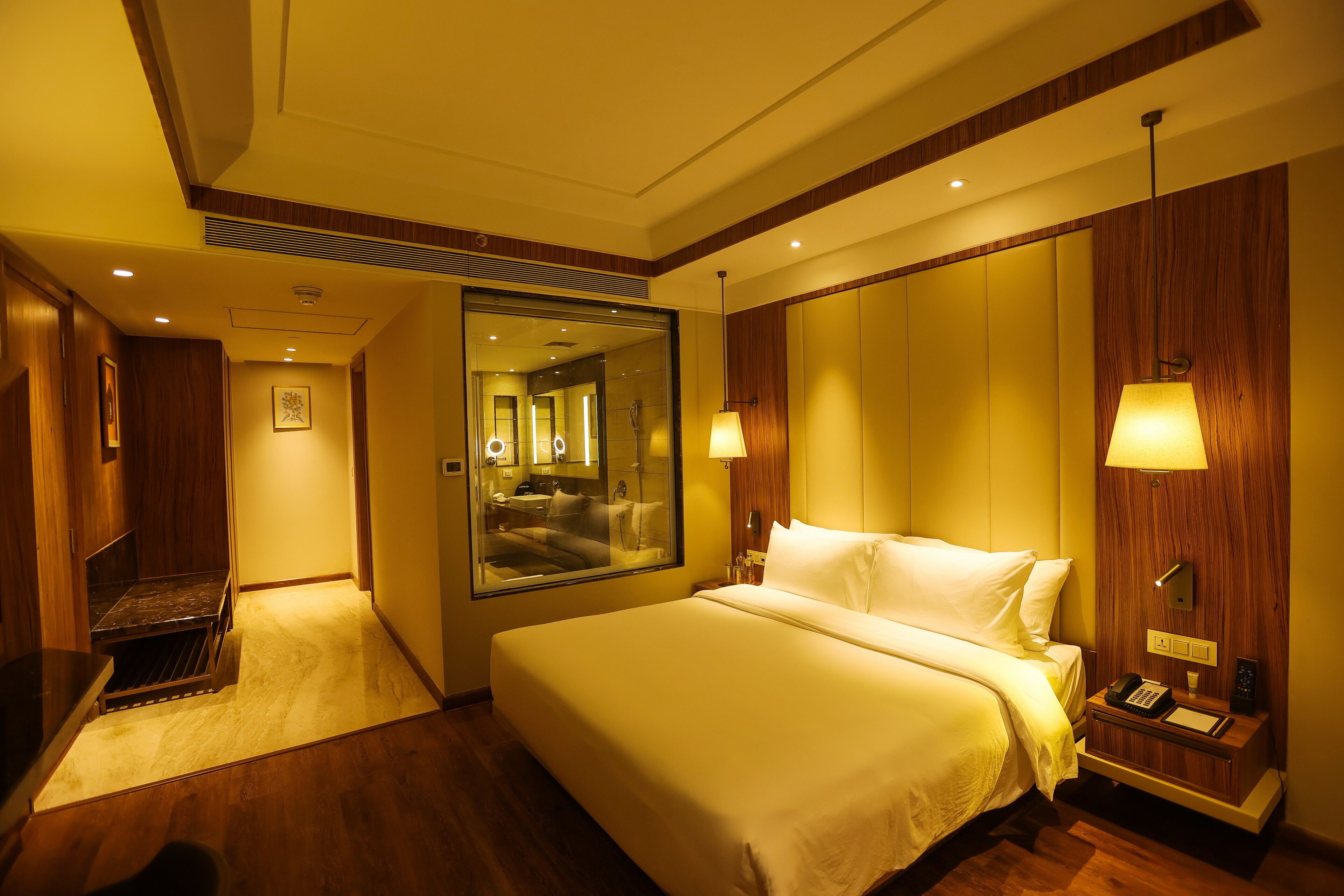 A hotel room with a large bed, a desk, a mirror, and a nightstand with a lamp.