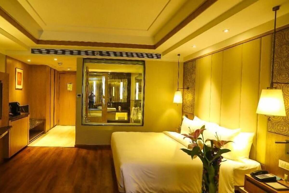 A hotel room with a bed, a TV, a mirror, and a desk with a lamp.