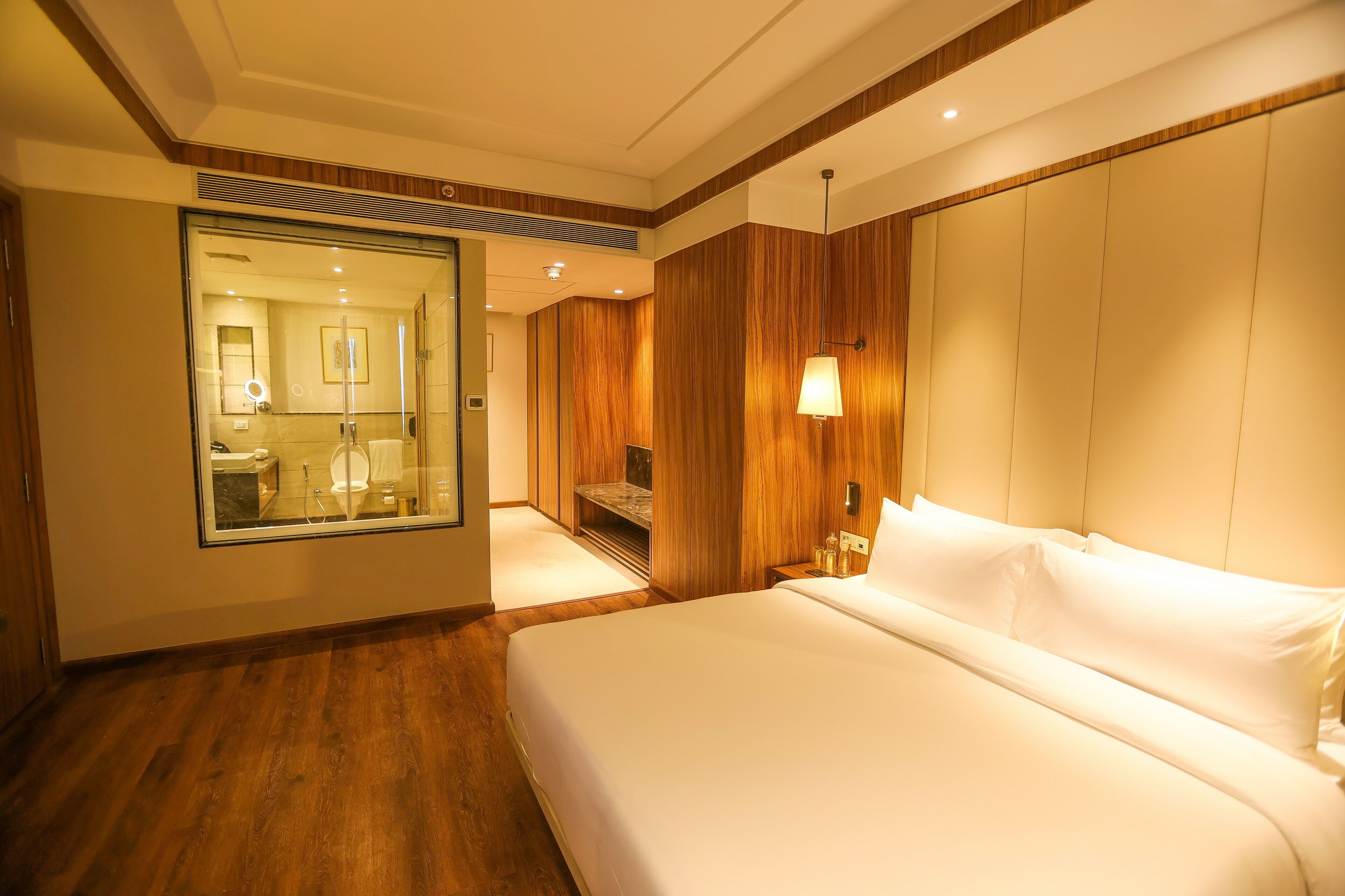 A hotel room with a large bed, wooden paneling, a mirror, and a nightstand with a lamp.