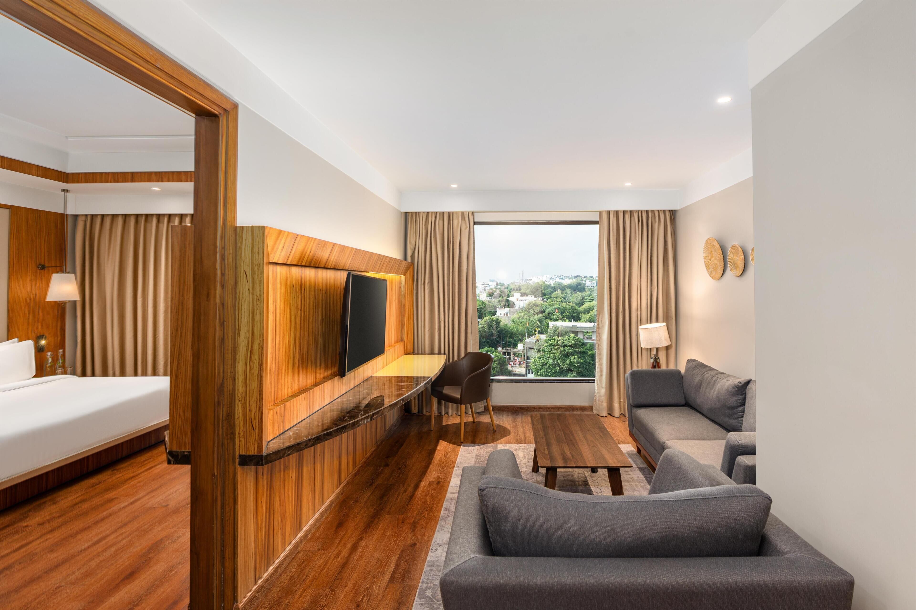 A hotel room with a bed, a desk, a sofa, and a large window with a city view.
