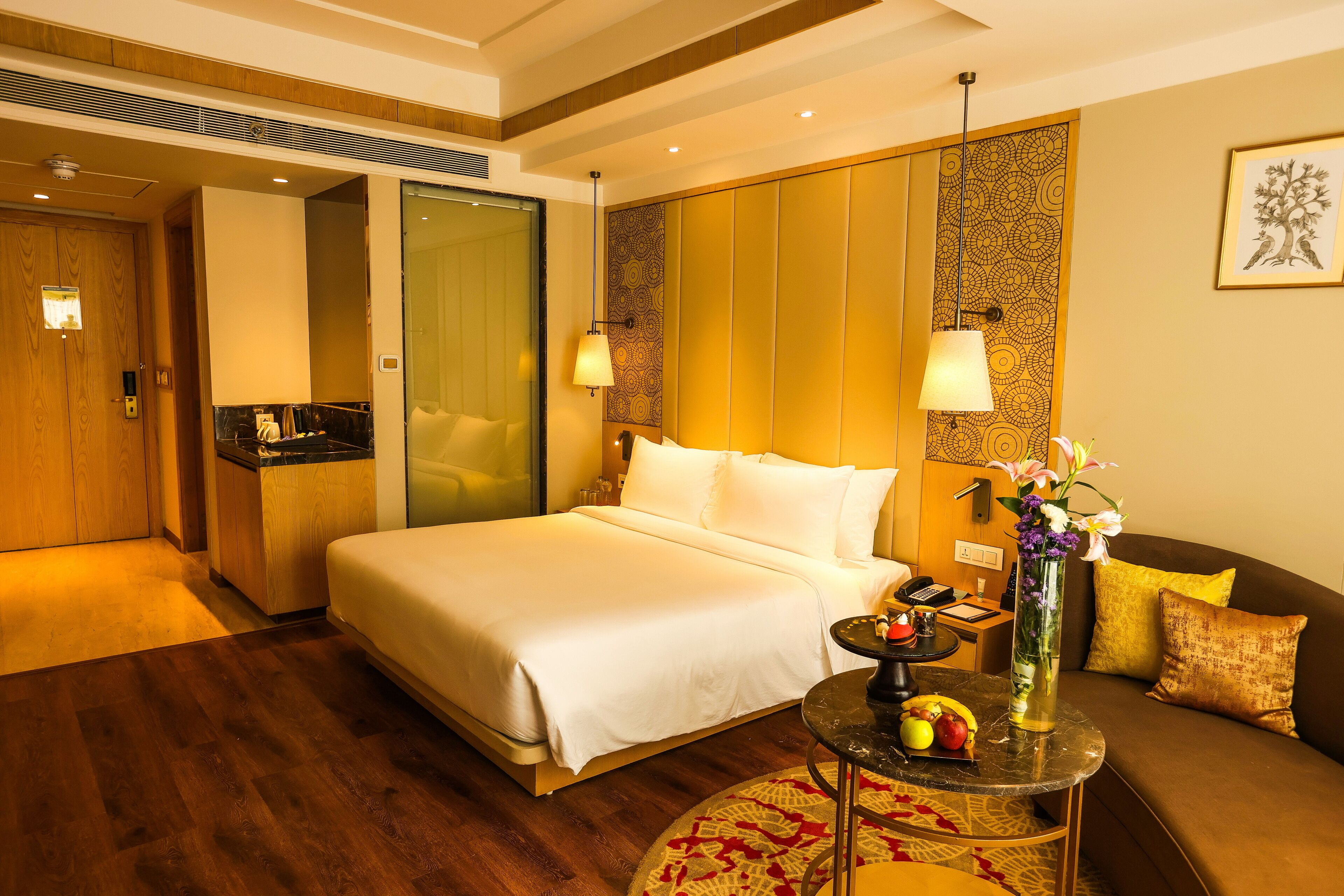 A hotel room with a large bed, a sofa, a small table with fruit, and a vase of flowers.