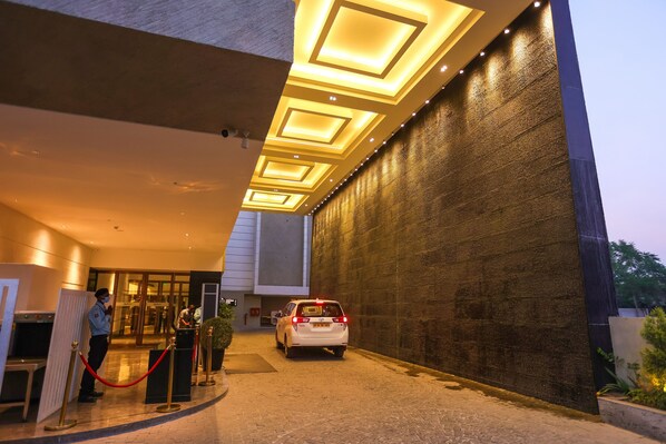 A modern building entrance with a white car parked in front, a security guard, and a red rope barrier. - Radisson Bhopal (Bhopal)