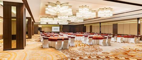 A conference room with rows of tables and chairs, a large chandelier, and a patterned carpet.