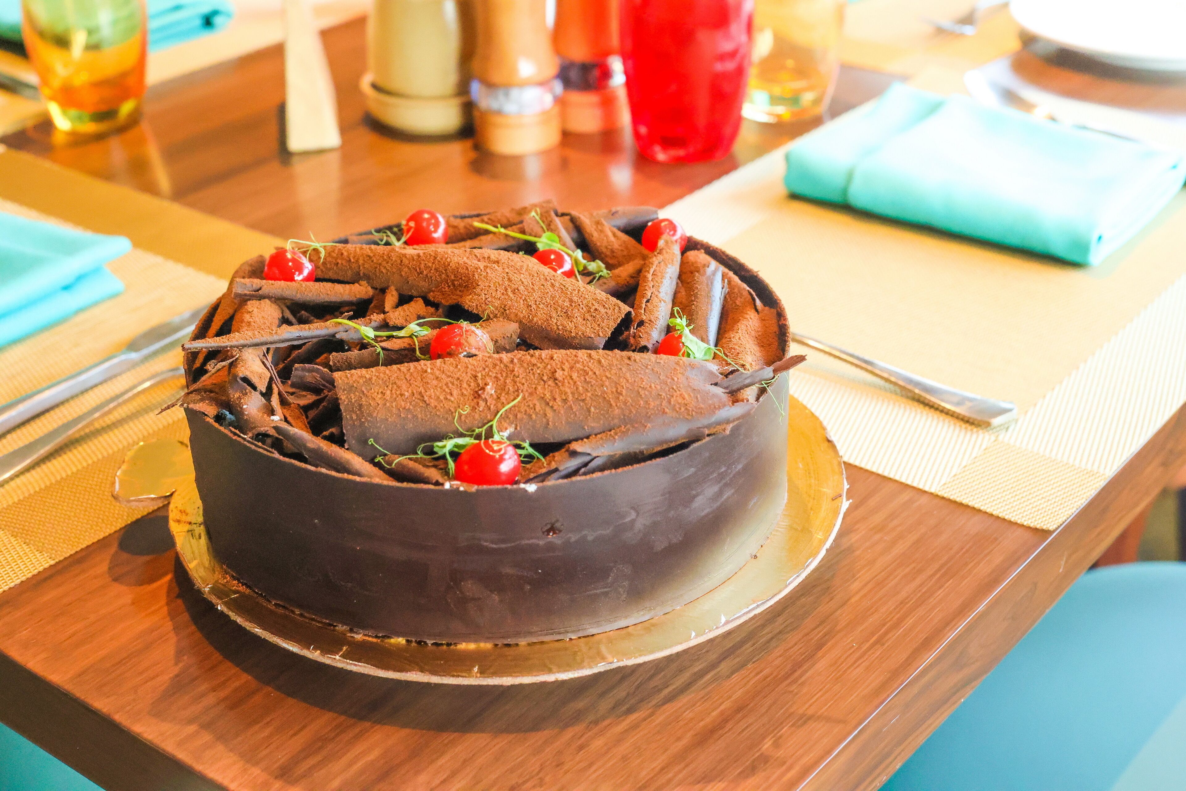 A chocolate cake with cherries and chocolate sticks on a wooden table.