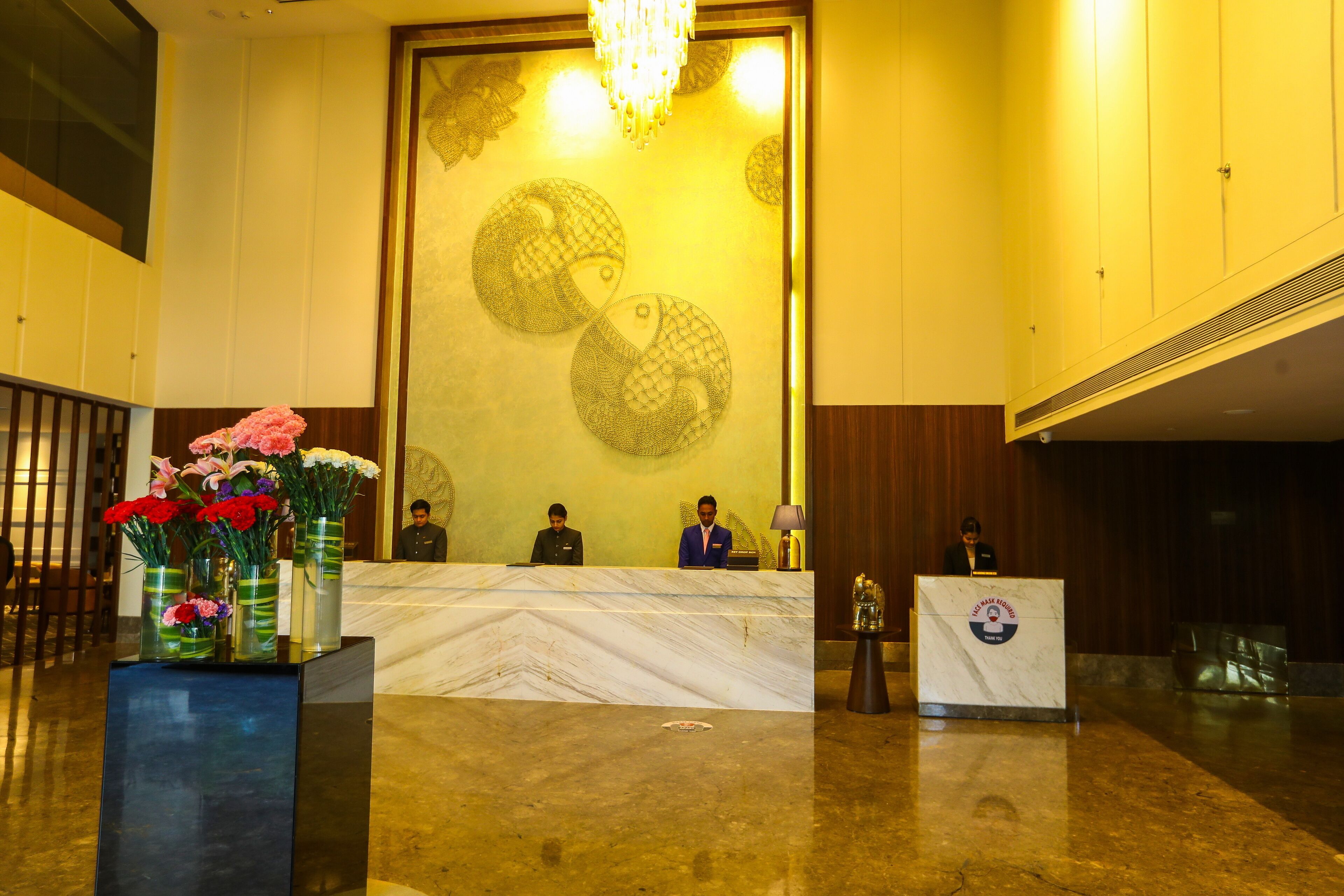 A reception area with a marble counter, floral arrangements, and a large decorative wall.