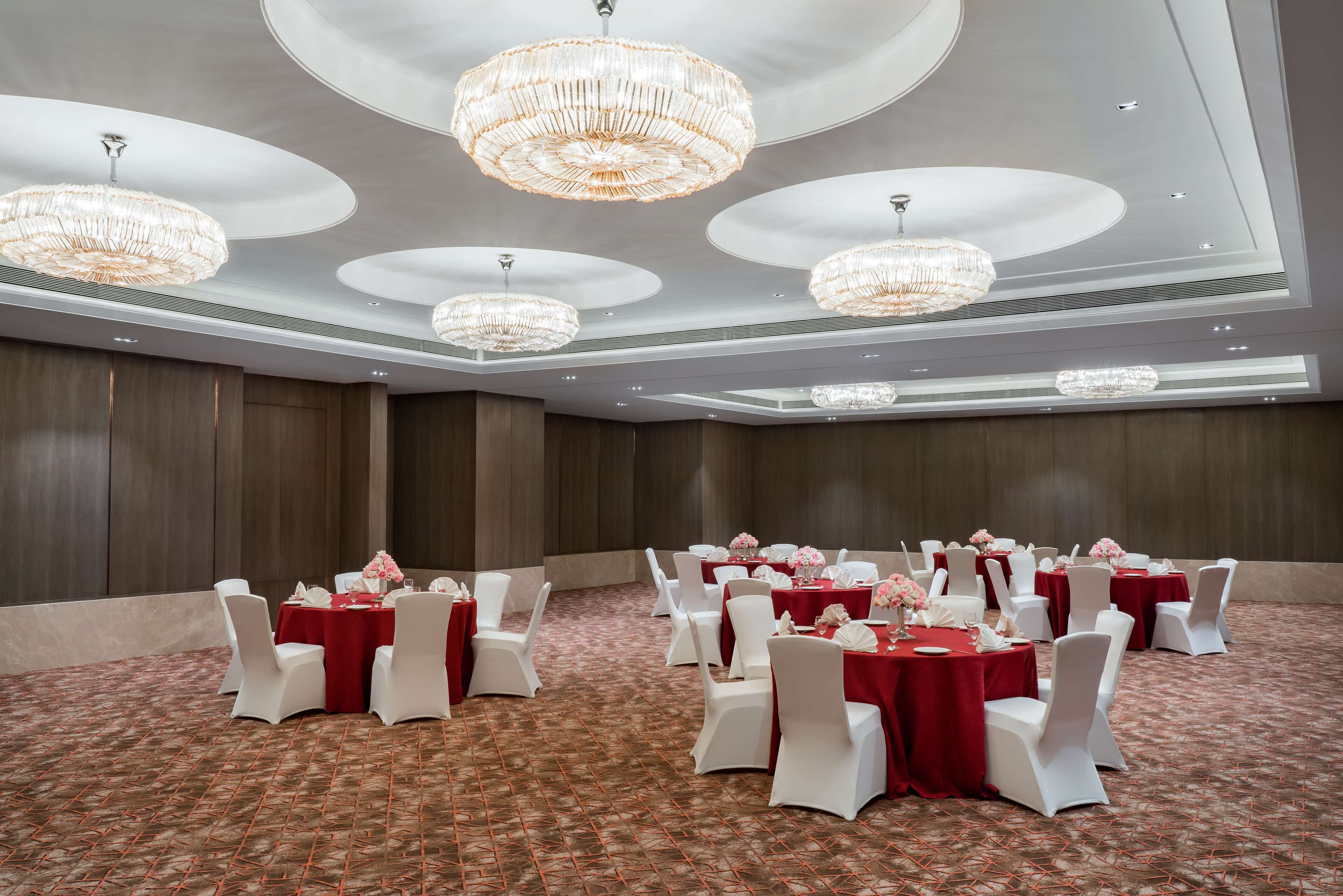 Una sala da banchetti con tavoli rotondi, sedie bianche e tovaglie rosse.