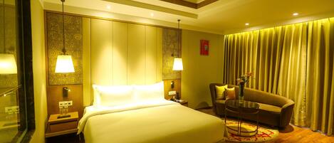 Une chambre d’hôtel avec un grand lit, un coin salon comprenant un fauteuil et une petite table, une table de chevet et un miroir.