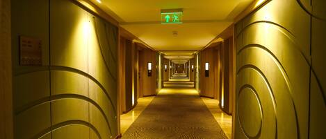 Un pasillo de hotel con alfombra estampada, paredes de madera y un letrero de salida de emergencia verde.
