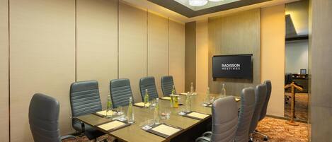 A conference room with a long table, six chairs, a television screen, and a patterned carpet.