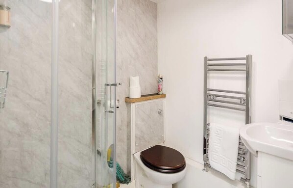 A bathroom with a glass shower enclosure, a toilet with a wooden seat, a towel rack, and a sink.