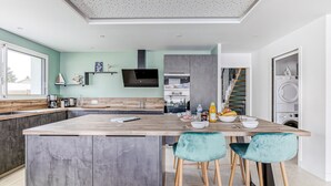 Een moderne keuken met een centraal eiland, barstoelen, een ingebouwde oven en een wasmachine in de aangrenzende kamer.