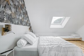 Een moderne slaapkamer met een schuine kap, dakraam, een bed met wit beddengoed en een wandplank met decoratieve objecten.