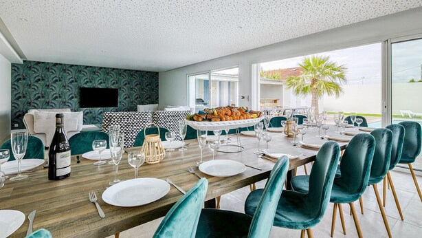 Een eetgedeelte met een lange tafel, gedekt voor een maaltijd, een fles wijn en een groot bord met eten.