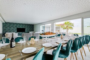 Een eetgedeelte met een lange tafel, gedekt voor een maaltijd, een fles wijn en een groot bord met eten.