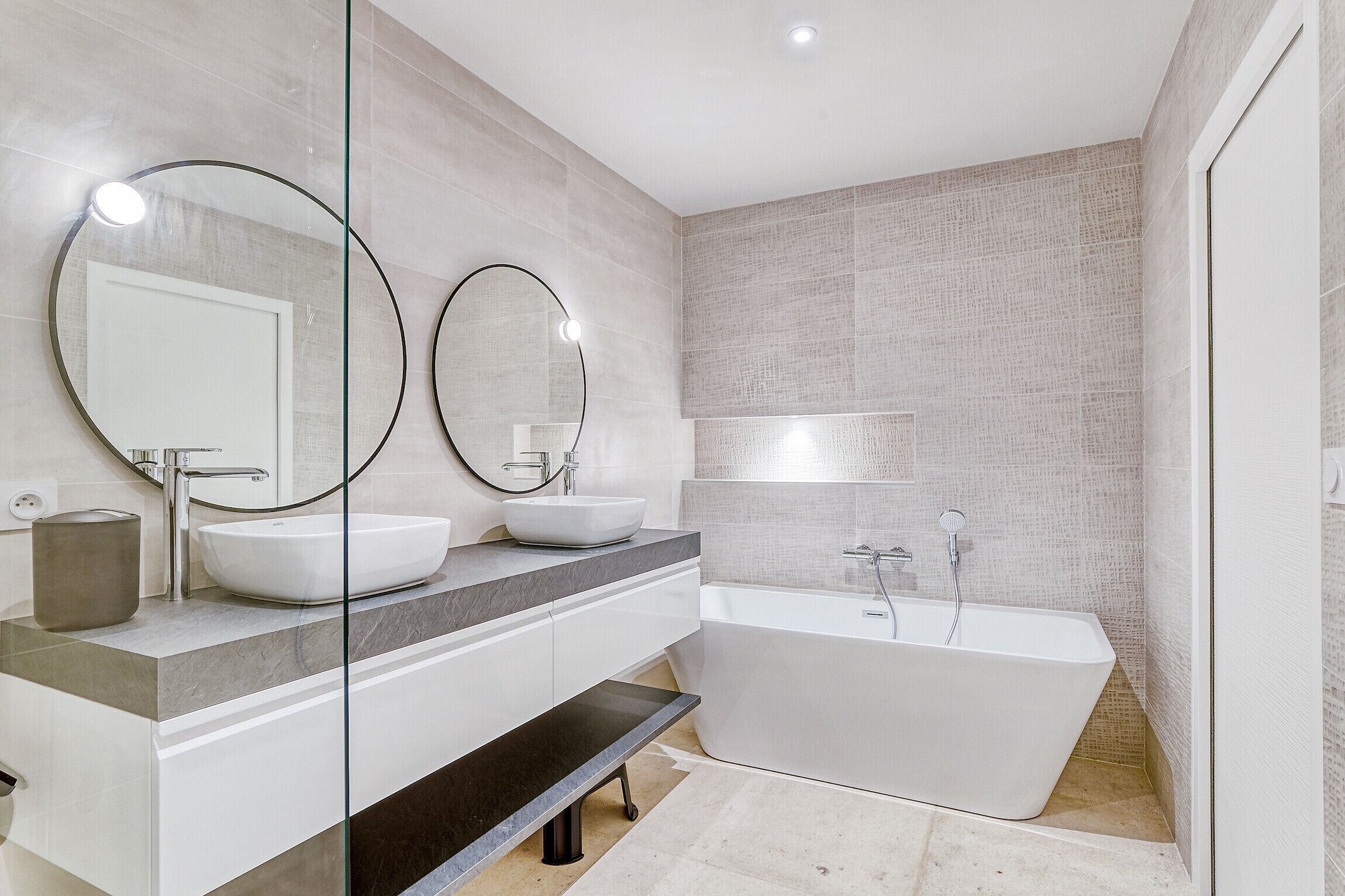 Une salle de bain moderne avec une baignoire sur pieds, un grand miroir et un meuble-lavabo doté d’un évier et d’un plan de travail.