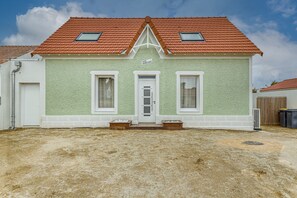 Een tweelaags huis met een rode pannendak, een groene gevel en een witte deur.