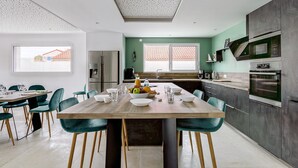 Een moderne keuken met een houten eettafel, teal-kleurige stoelen en roestvrijstalen apparatuur.
