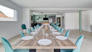 Een eetgedeelte met een lange houten tafel voor zes personen, teal stoelen en een keuken op de achtergrond.
