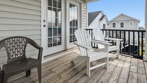 Une terrasse en bois avec deux fauteuils Adirondack et un banc, une porte blanche avec un panneau de verre, et une vue sur les maisons voisines.