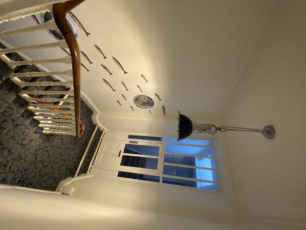 A staircase with a white railing, a patterned carpet, a ceiling light fixture, and a window with blinds.