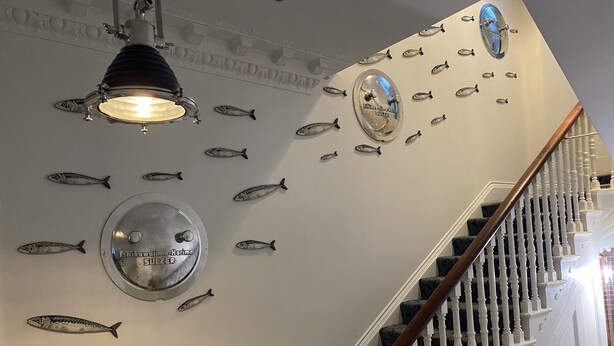 En trappe med et trægelænder og hvide spjæld, omgivet af vægge med fiskedekorationer og et loftlys.