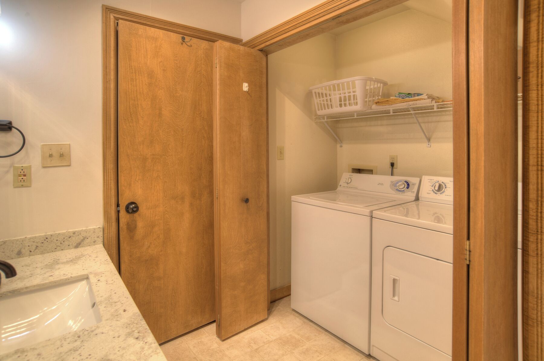 A laundry room with two washers and dryers, a wooden door, and a countertop with a sink.