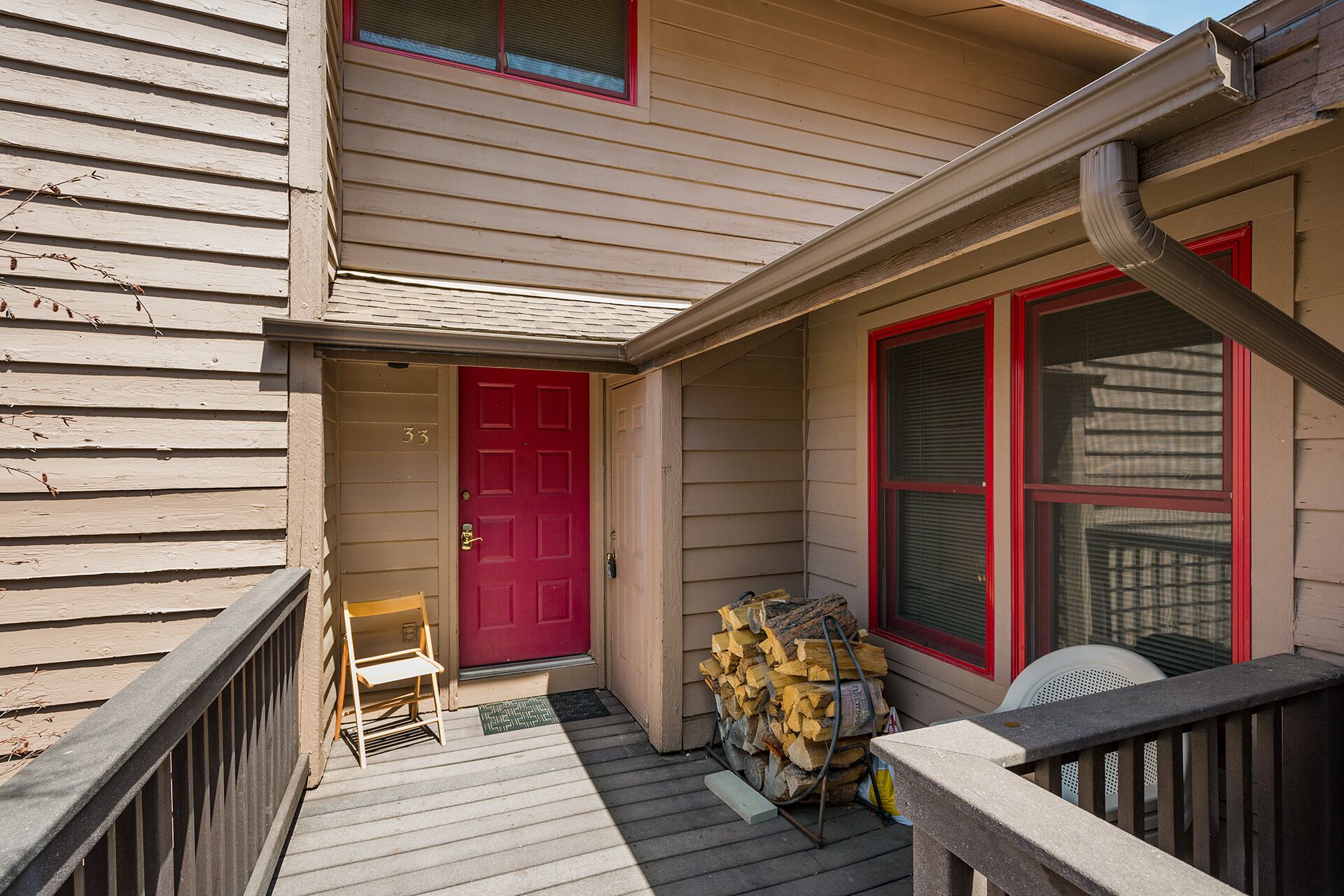 A wooden house with a red door, a porch with a chair, and a stack of firewood.