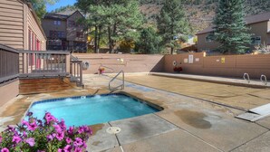 Zona de piscina con plataforma de madera, escalera metálica y vistas a edificios y árboles circundantes.