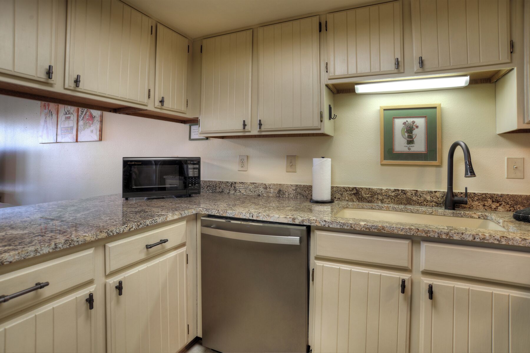 A kitchen with beige cabinets, a black microwave, a sink, and a dishwasher.