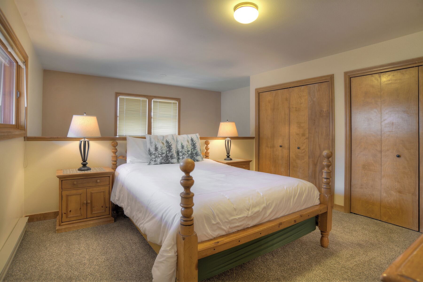 A bedroom with a wooden bed, two bedside tables with lamps, a large mirror, and a wardrobe.