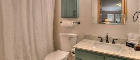 Un bagno con il water bianco, una tenda da doccia, un lavandino con uno specchio sopra e un asciugamano appeso al muro.