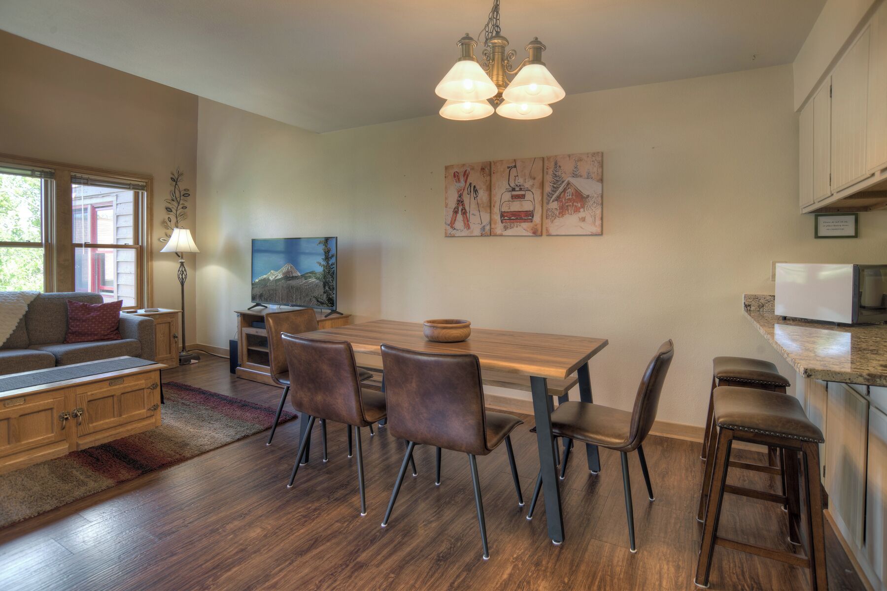 A dining area with a wooden table and chairs, a television, and artwork on the wall.