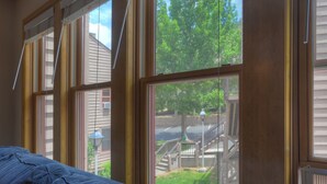 A room with large windows, a bed, and a view of a backyard with a wooden deck and trees. - The Blue Bear | Trails, Golf, Pool & Hot Tub - Near Town (Durango)