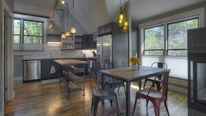 A modern kitchen with a wooden table and chairs, stainless steel appliances, and large windows.