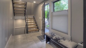 A staircase with wooden steps and metal railings, leading to a door with a view of greenery outside.