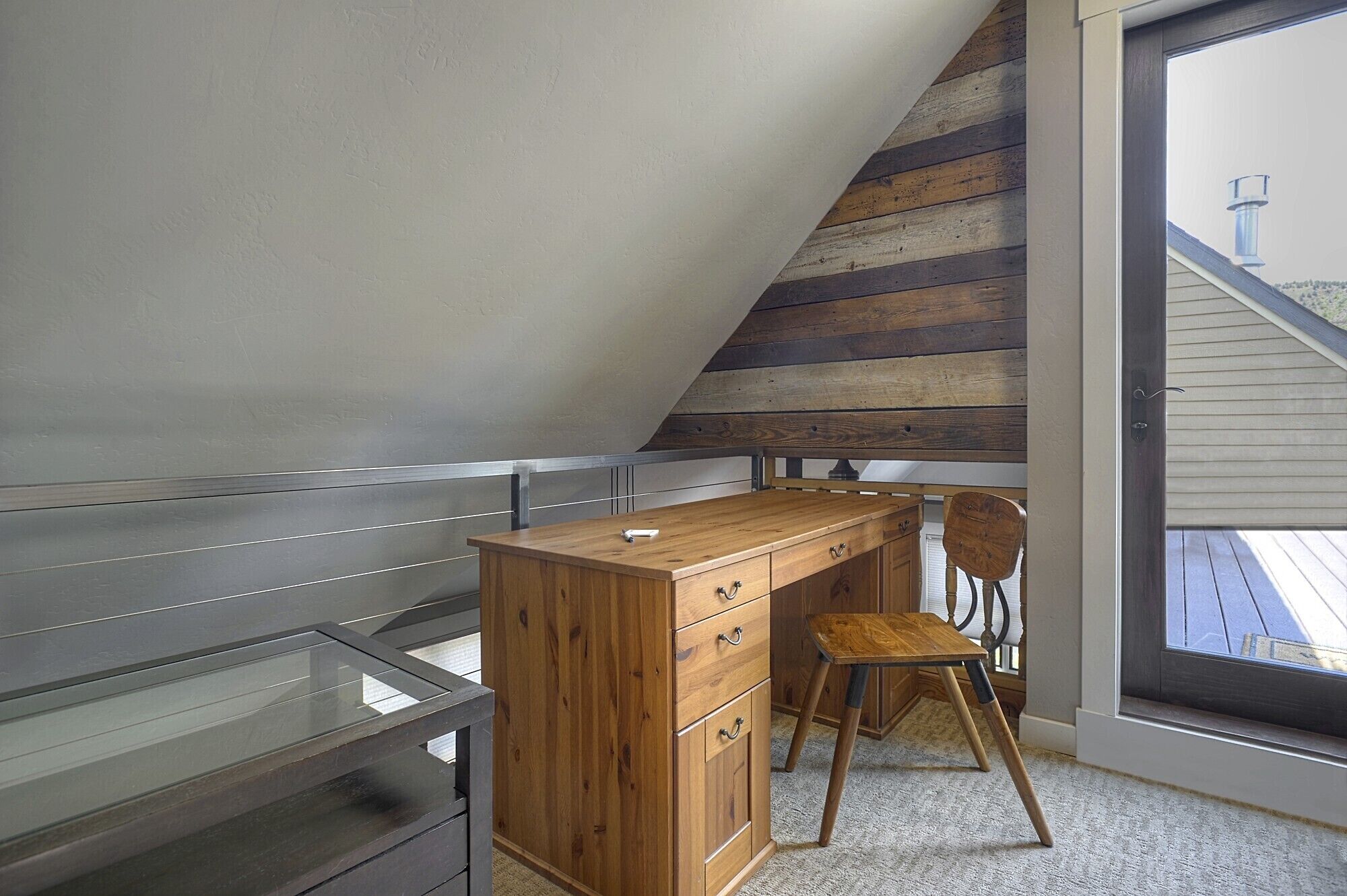 A small attic bedroom with a wooden desk and chair, a window, and a view of the outside.