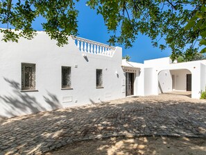 A white building with a cobblestone courtyard, a balcony, and a door with a decorative arch.