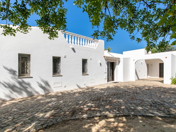 A white building with a cobblestone courtyard, a balcony, and a door with a decorative arch.