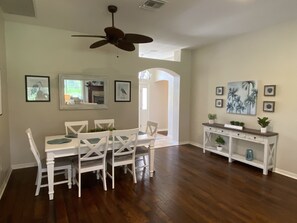 Uma área de jantar com uma mesa e cadeiras brancas, um ventilador de teto e um aparador com plantas.