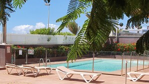 A swimming pool with lounge chairs, surrounded by a fence and greenery.