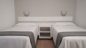 A hotel room with two single beds, a small desk, and a wall-mounted light fixture.