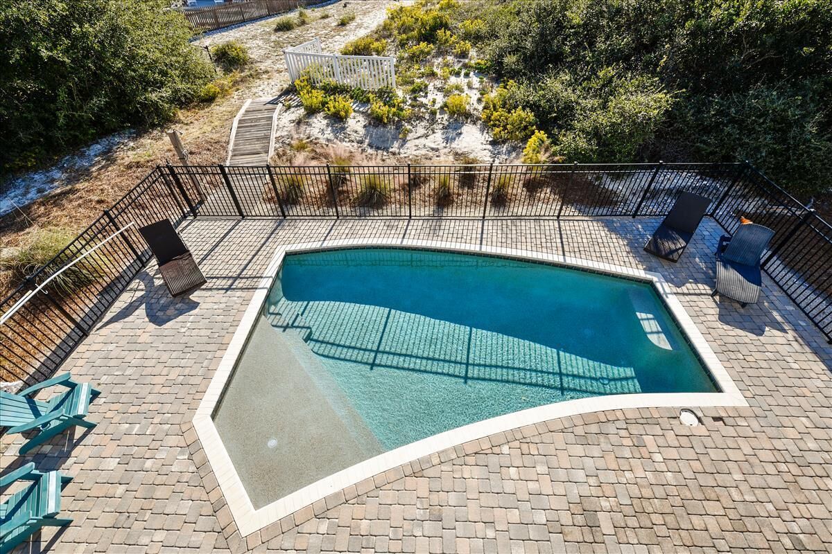 Une piscine à bord incurvé, entourée d’une terrasse en briques et d’une clôture en métal.
