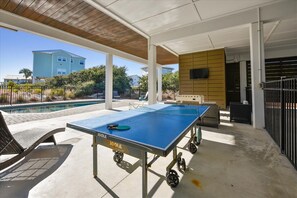 Une table de billard recouverte d’un drap bleu, un fauteuil et une petite table sur laquelle se trouve un téléviseur.